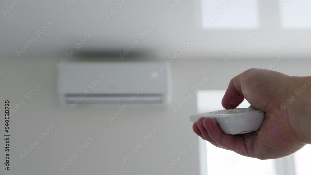 The man's hand holds the remote control from the air conditioner in his