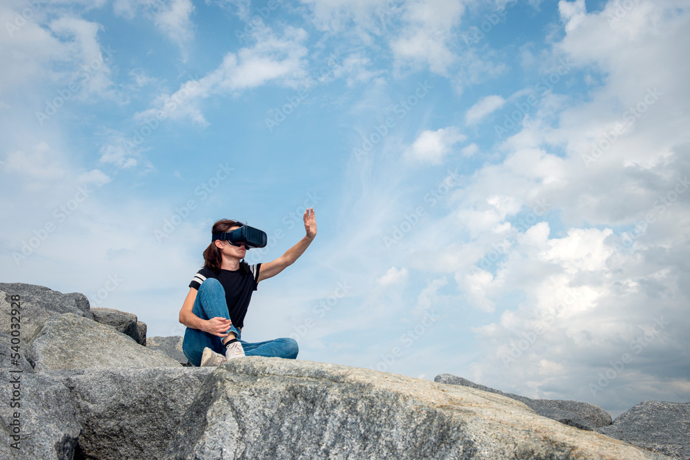 Woman wearing a VR headset reaching out to the sky. Woman wearing a VR headset reaching out to the sky.