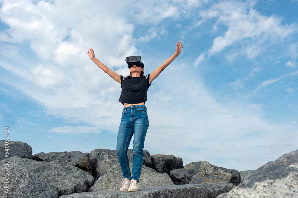 Woman wearing a VR headset reaching out to the sky. Woman wearing a VR headset reaching out to the sky.