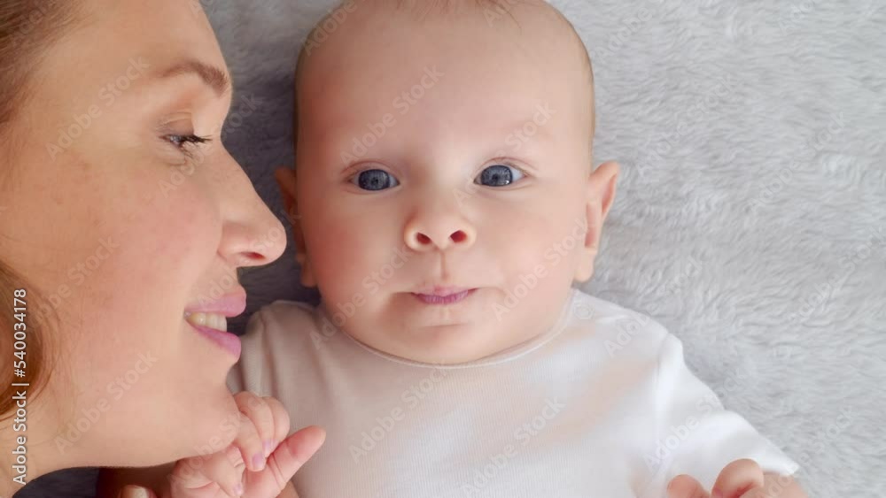 Happy newborn baby with his mother. Closeup Faces of the mother and infant baby. Healthy newborn baby in a white t-shirt with mom. Cute Infant boy and parent, top view. Slow motion. Happy family Happy newborn baby with his mother. Closeup Faces of the mother and infant baby. Healthy newborn baby in a white t-shirt with mom. Cute Infant boy and parent, top view. Slow motion. Happy family