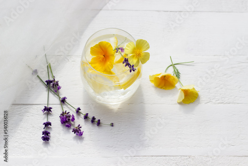 Homemade lemonade in a glass on the white wood table with yellow flowers and lavener with tulle fabric on the background