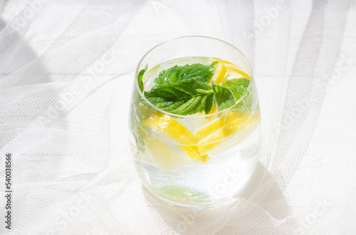 Close-up of homemade lemonade with lemon, mint and ice cubes in a glass on white wood table with white tulle fabric