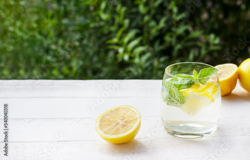 Homemade lemonade with lemon, mint and ice cubes in a glass on the white wood table with lemons.