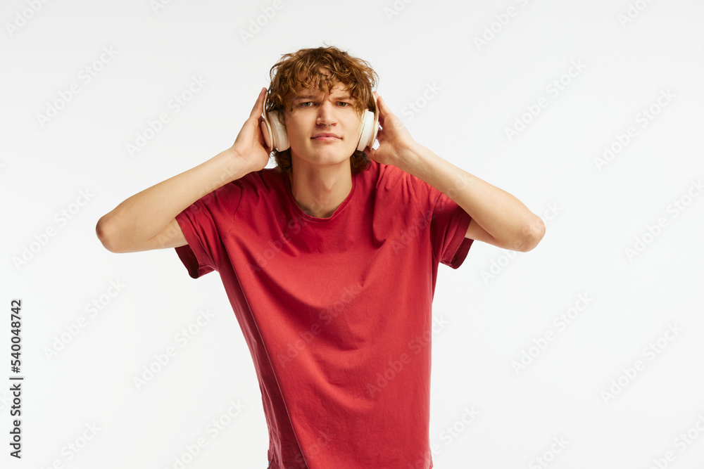 One young man, student in red tee and headphones isolated on white background. Concept of emotions, facial expression, youth and remote studying One young man, student in red tee and headphones isolated on white background. Concept of emotions, facial expression, youth and remote studying