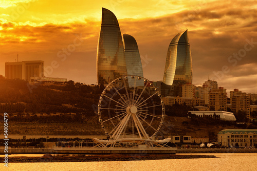 Ferris wheel and skyscrapers against cloudy sky at sunset time in Baku
