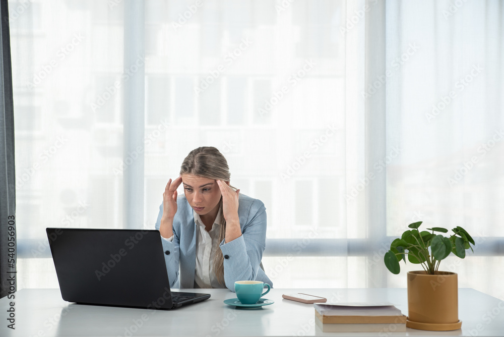 Exhausted upset young business woman sitting at table with laptop, leaning head on hand, suffering from headache, feeling depressed, unhappy, tired, getting bad news. Professional burnout concept Exhausted upset young business woman sitting at table with laptop, leaning head on hand, suffering from headache, feeling depressed, unhappy, tired, getting bad news. Professional burnout concept