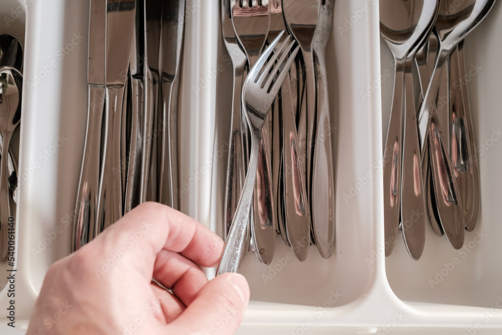 Male hand takes a fork from a drawer with cutlery. Close-up. Male hand takes a fork from a drawer with cutlery. Close-up.