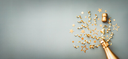 Golden champagne bottle with confetti stars and party decorations on blue background. Christmas, birthday or New Year card.