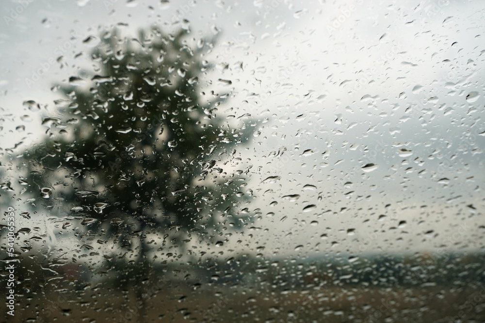 Fensterscheibe mit Regentropfenmuster vor Baum, Ackerfelder, Haus und Himmel bei Regen am Nachmittag im Herbst