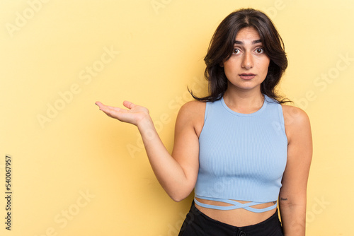 Young Indian woman isolated on yellow background impressed holding copy space on palm.