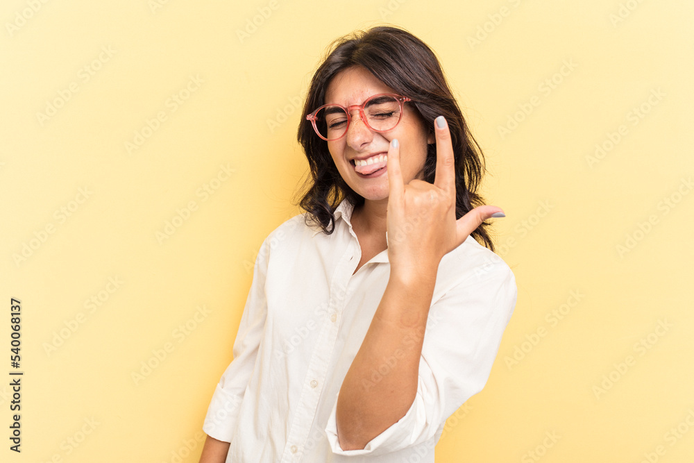 Young Indian woman isolated on yellow background showing rock gesture with fingers Young Indian woman isolated on yellow background showing rock gesture with fingers