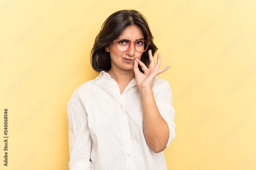 Young Indian woman isolated on yellow background with fingers on lips keeping a secret. Young Indian woman isolated on yellow background with fingers on lips keeping a secret.