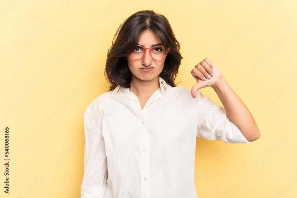 Young Indian woman isolated on yellow background showing thumb down, disappointment concept. Young Indian woman isolated on yellow background showing thumb down, disappointment concept.
