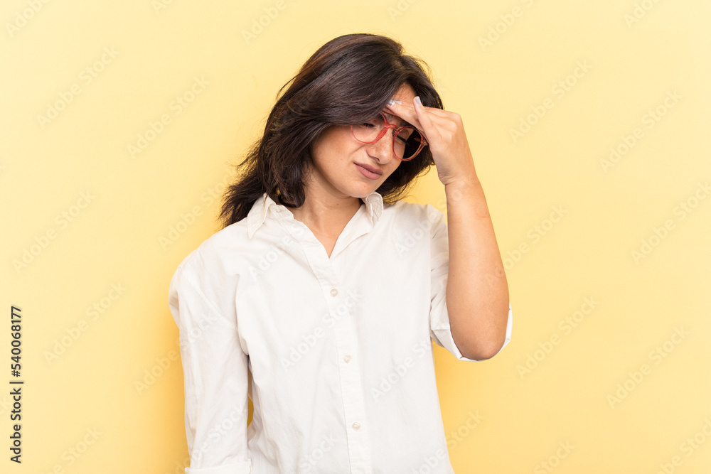 Young Indian woman isolated on yellow background having a head ache, touching front of the face.