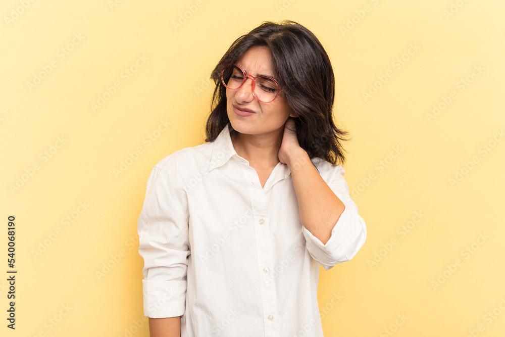 Young Indian woman isolated on yellow background having a neck pain due to stress, massaging and touching it with hand. Young Indian woman isolated on yellow background having a neck pain due to stress, massaging and touching it with hand.