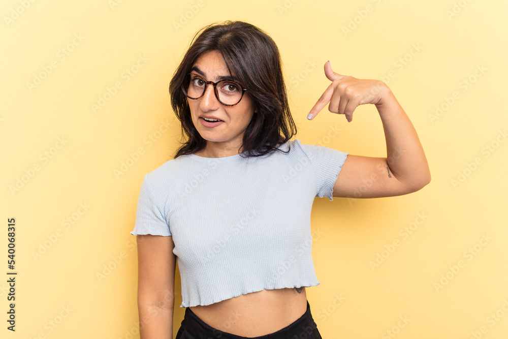 Young Indian woman isolated on yellow background person pointing by hand to a shirt copy space, proud and confident