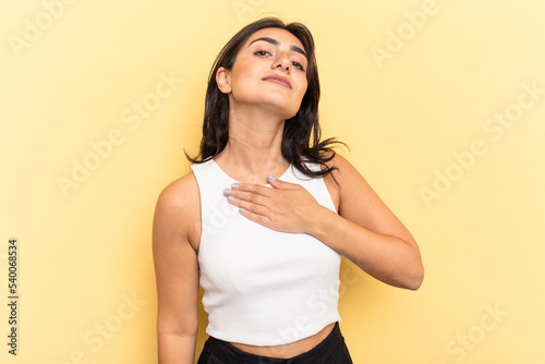 Young Indian woman isolated on yellow background taking an oath, putting hand on chest.