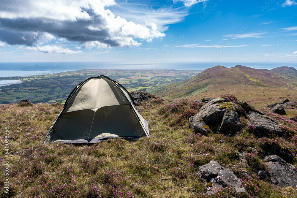 Small tent on the top of mountain during summer time. Epic view on the sea and fields. Outdoor activity concept.