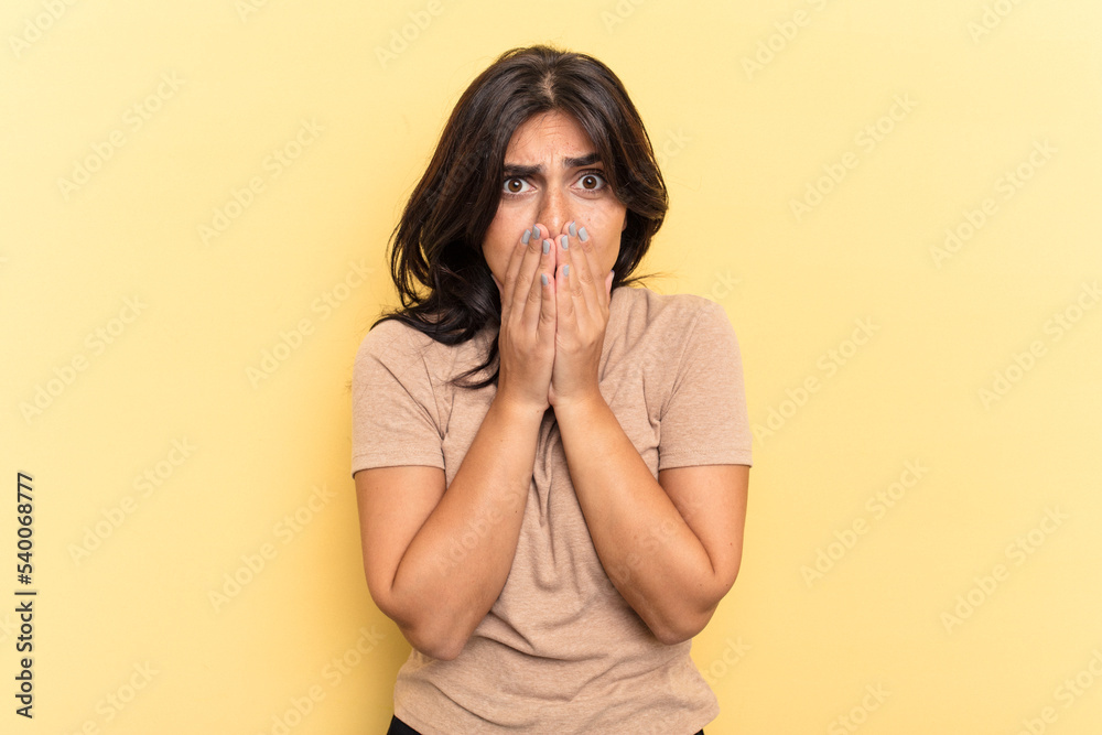 Young Indian woman isolated on yellow background covering mouth with hands looking worried. Young Indian woman isolated on yellow background covering mouth with hands looking worried.