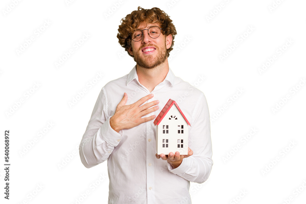 Business caucasian man holding toy house isolated on white background laughs out loudly keeping hand on chest. Business caucasian man holding toy house isolated on white background laughs out loudly keeping hand on chest.
