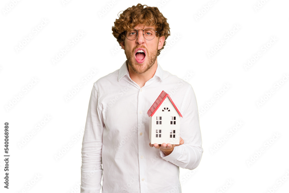 Business caucasian man holding toy house isolated on white background screaming very angry and aggressive. Business caucasian man holding toy house isolated on white background screaming very angry and aggressive.