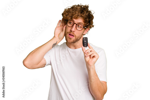 Young caucasian man holding car keys isolated on white background trying to listening a gossip. © Asier