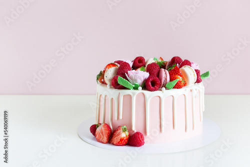 Beautiful pink cake decorated with macarons, raspberries, strawberries and sugar rose flowers.
