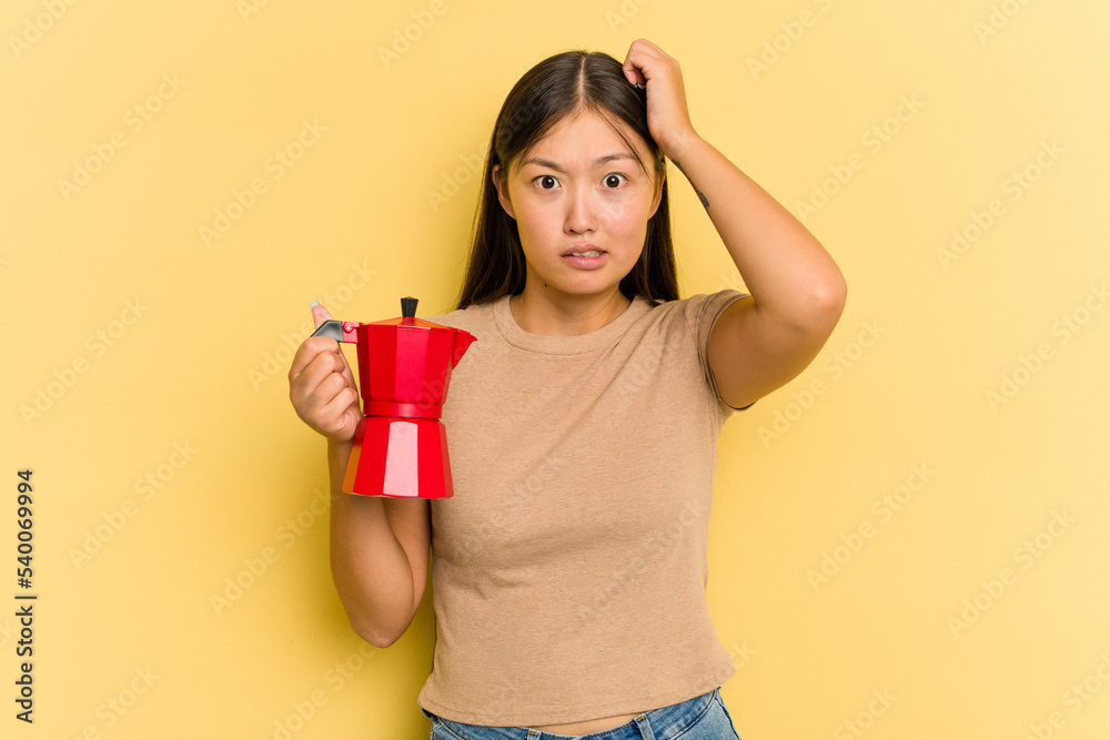 Obraz premium Young Asian woman holding coffee maker isolated on yellow background being shocked, she has remembered important meeting.