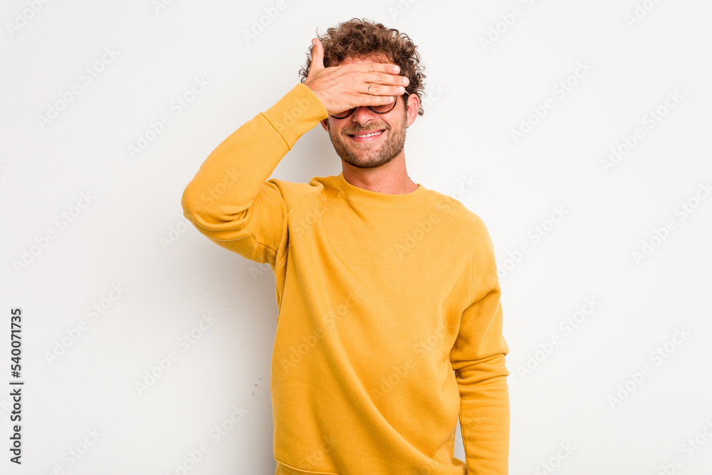 Fototapeta premium Young caucasian curly hair man isolated on white background covers eyes with hands, smiles broadly waiting for a surprise.