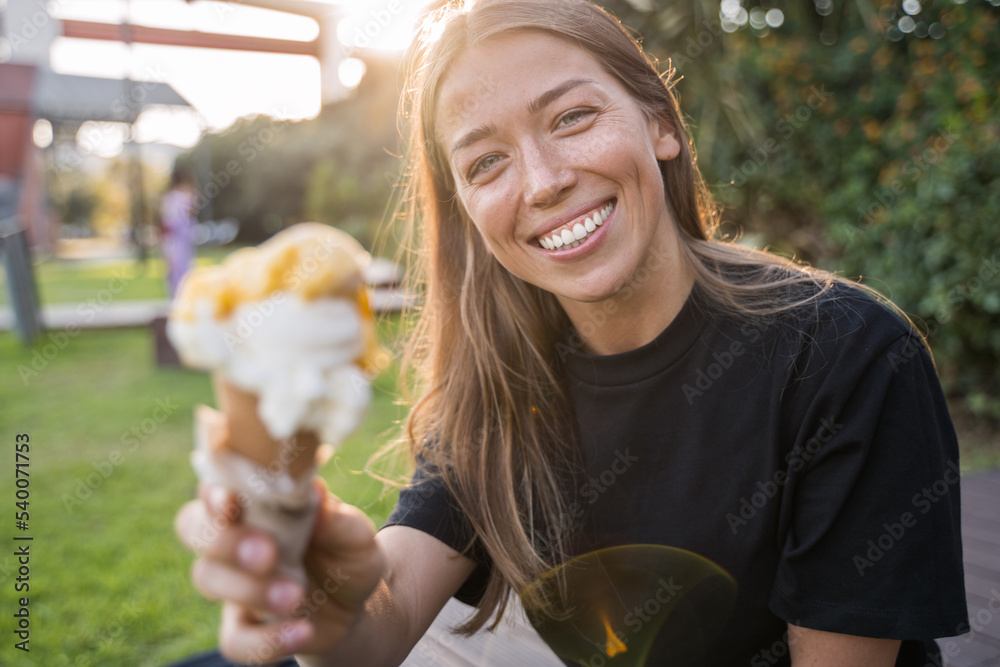 Fototapeta premium Happy teen woman relaxing with ice cream on bench in the park