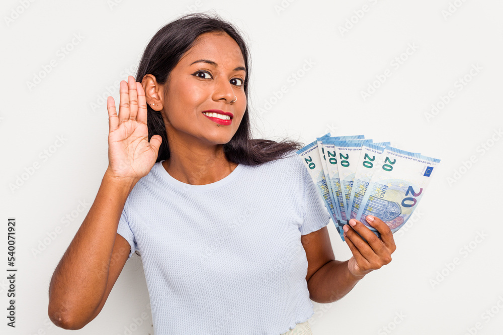 Young indian woman holding a banknotes isolated on white background trying to listening a gossip. Young indian woman holding a banknotes isolated on white background trying to listening a gossip.