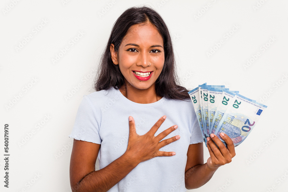 Young indian woman holding a banknotes isolated on white background laughs out loudly keeping hand on chest. Young indian woman holding a banknotes isolated on white background laughs out loudly keeping hand on chest.