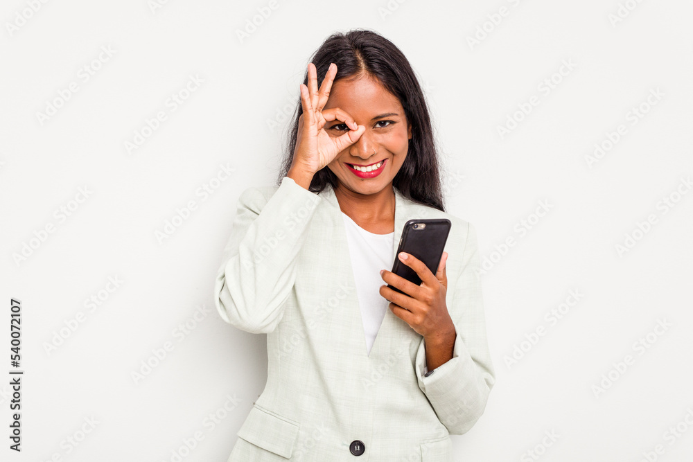 Young business Indian woman holding a mobile phone isolated on white background excited keeping ok gesture on eye. Young business Indian woman holding a mobile phone isolated on white background excited keeping ok gesture on eye.
