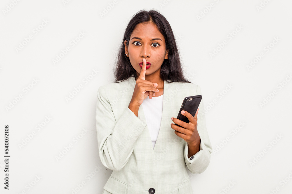 Young business Indian woman holding a mobile phone isolated on white background keeping a secret or asking for silence. Young business Indian woman holding a mobile phone isolated on white background keeping a secret or asking for silence.