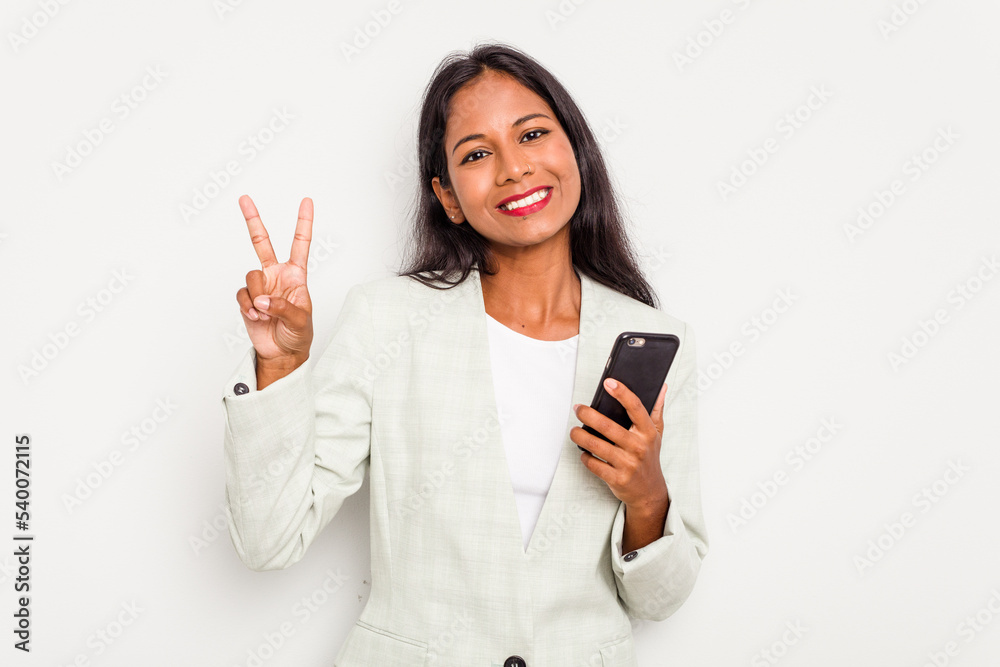 Young business Indian woman holding a mobile phone isolated on white background joyful and carefree showing a peace symbol with fingers. Young business Indian woman holding a mobile phone isolated on white background joyful and carefree showing a peace symbol with fingers.