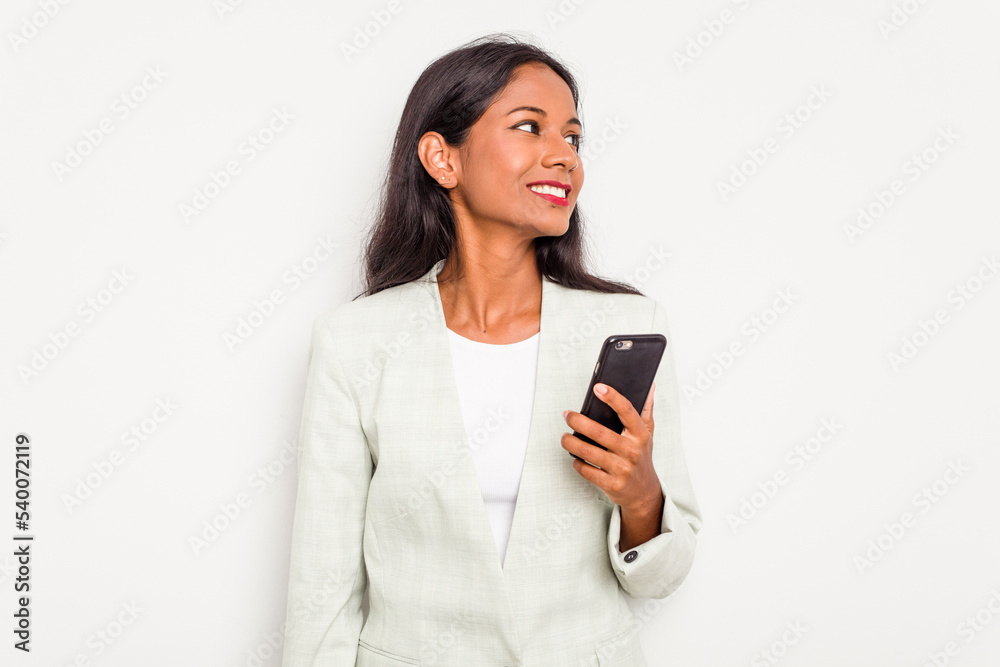 Young business Indian woman holding a mobile phone isolated on white background looks aside smiling, cheerful and pleasant.