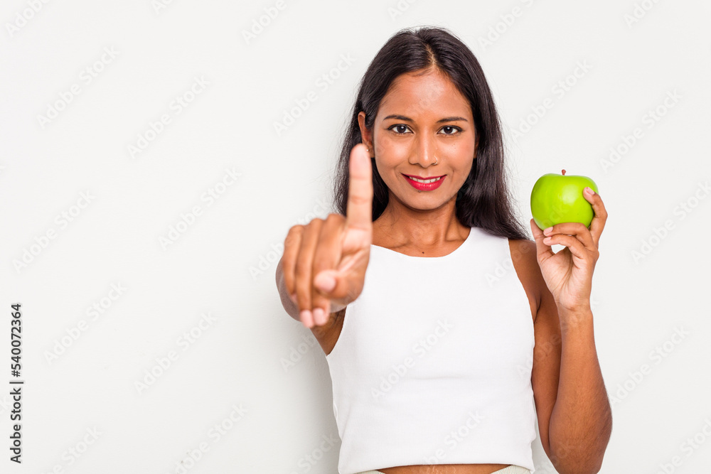 Young Indian woman holding an apple isolated on white background showing number one with finger. Young Indian woman holding an apple isolated on white background showing number one with finger.