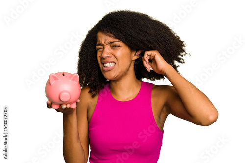 Young African American woman holding a piggy bank isolated covering ears with hands.