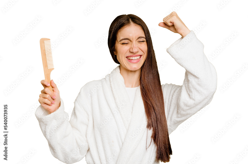 Young caucasian woman holding an hair comb isolated raising fist after a victory, winner concept.