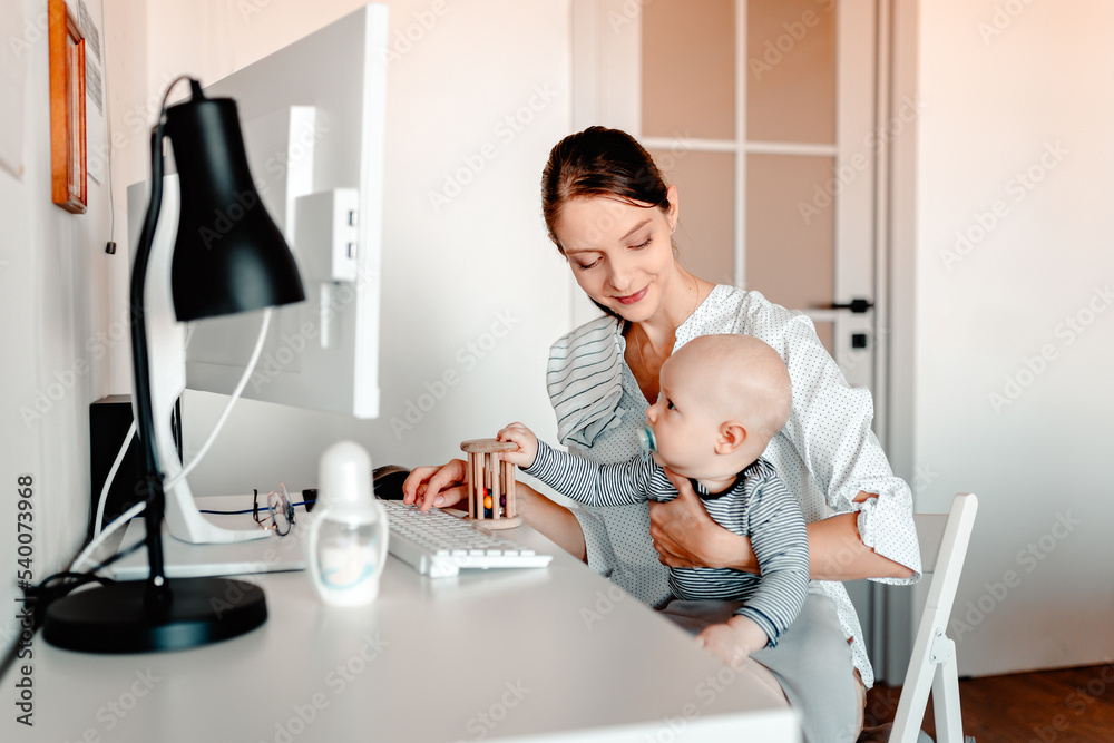 Mother working on computer with baby in hands. Working mother with kid.