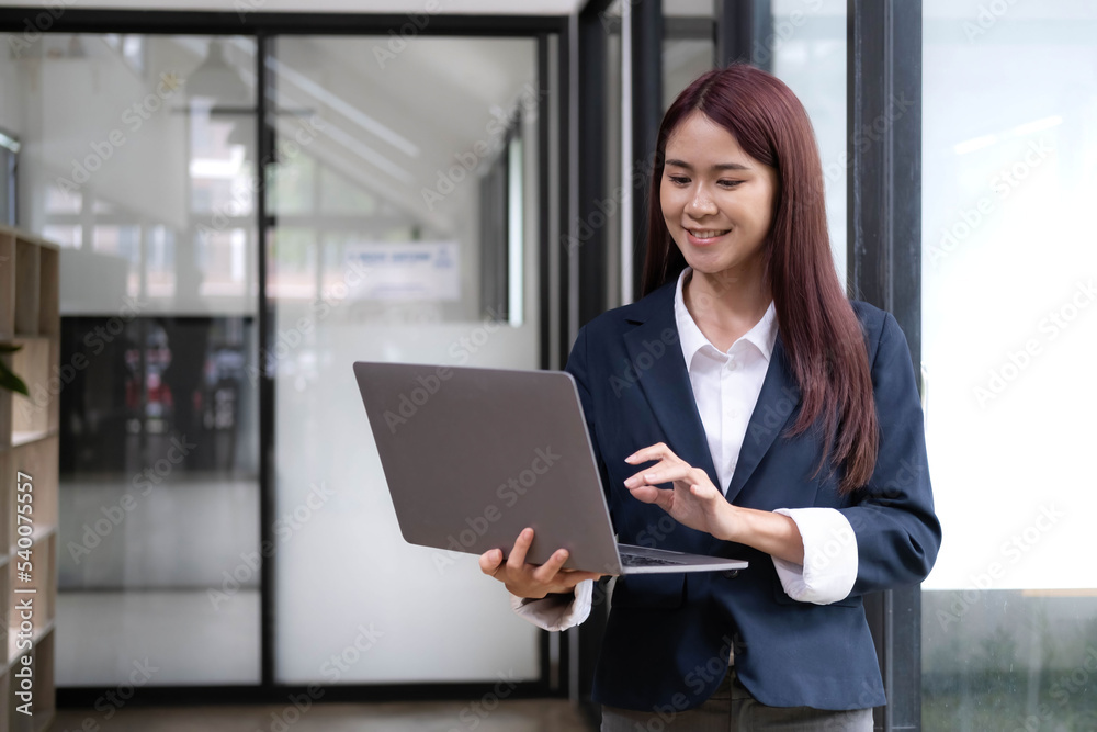 Attractive young asian woman using laptop computer while standing in a office. Attractive young asian woman using laptop computer while standing in a office.