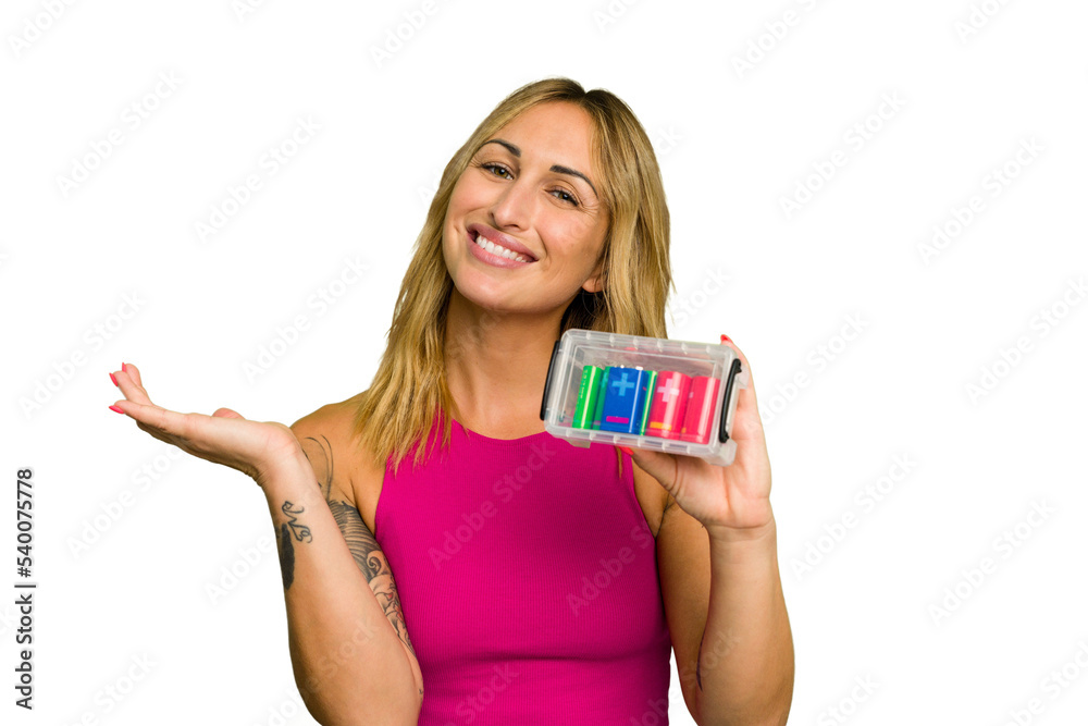 Young caucasian woman holding battery box isolated on green chroma background showing a copy space on a palm and holding another hand on waist. Young caucasian woman holding battery box isolated on green chroma background showing a copy space on a palm and holding another hand on waist.