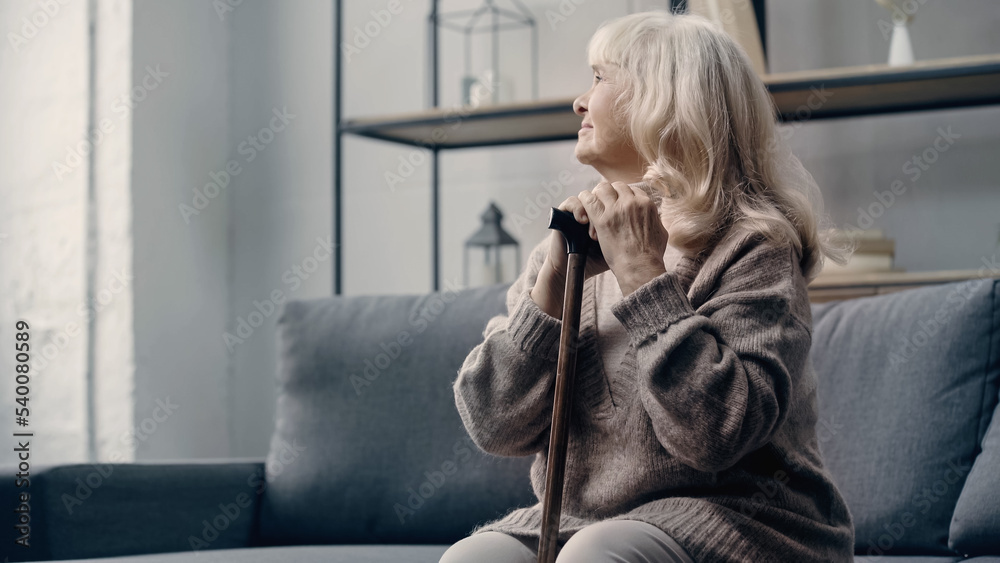 Obraz premium senior woman with dementia sitting on sofa with walking stick.