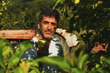 Portrait of a middle eastern holding an apple in his hand and posing in an apple orchard with a tractor on the background.