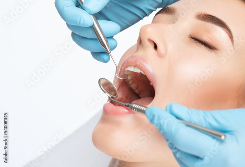 A dentist doctor treats caries on a tooth of a young beautiful woman in a dental clinic. Tooth filling. photo