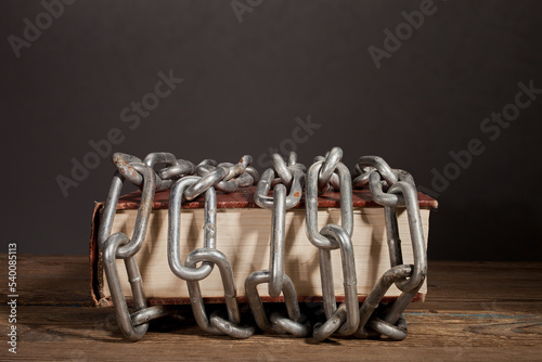 The book is in chains. Books wrapped in a chain on a wooden table.
