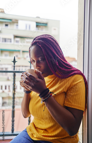 african american woman drinking coffee sitting at kitchen window photo