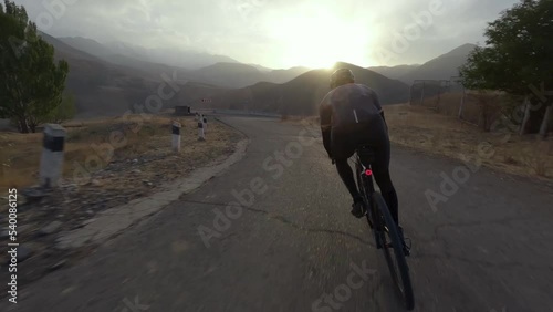 Aerial view athletic sportsman riding asphalt serpentine road sports bike at sunset mountain valley landscape. FPV sport drone shot active man cycling extreme outdoor leisure activity cliff scenery 4k