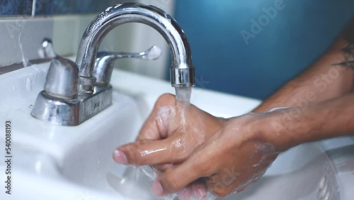 Hombre delgado caucasico lavandose las manos en un grifo de baño  photo