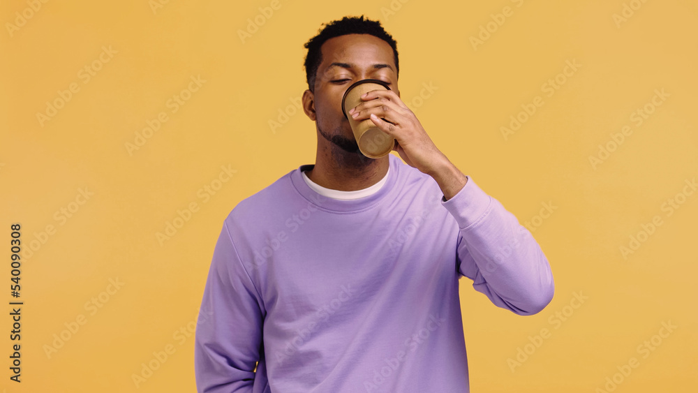 african american man in purple pullover drinking coffee to go isolated on yellow. african american man in purple pullover drinking coffee to go isolated on yellow.